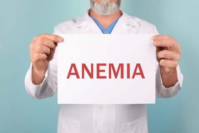 Image of Doctor holding sign with word ANEMIA on color background, closeup