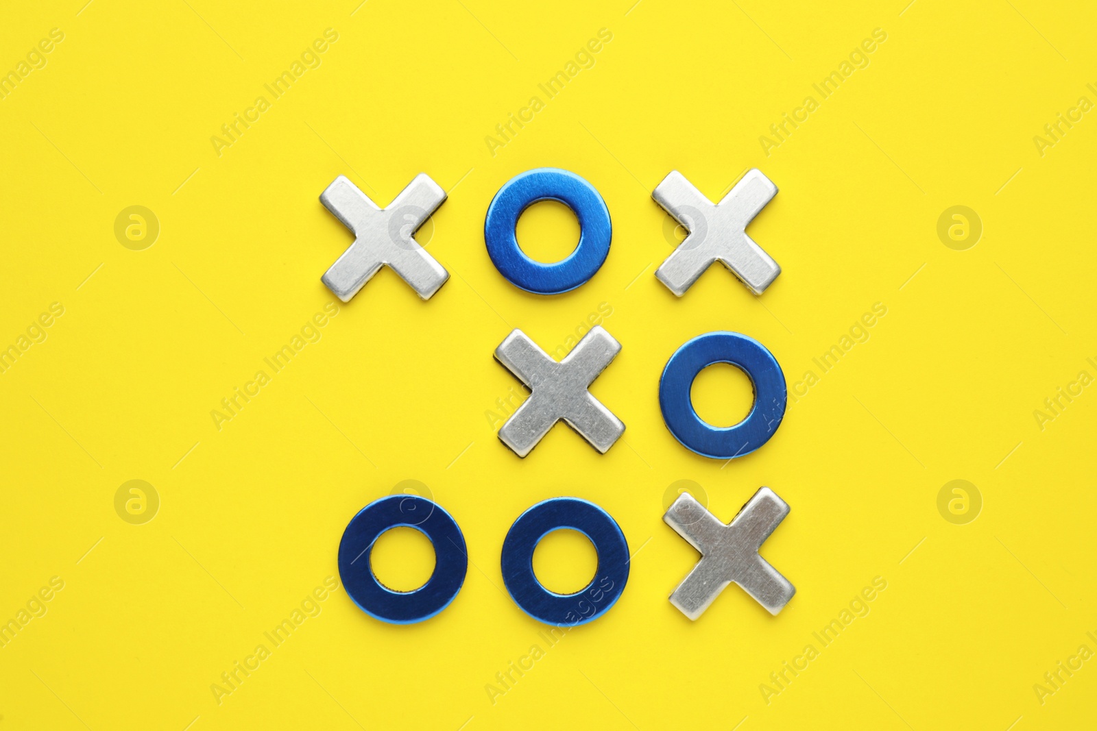 Photo of Metallic tic-tac-toe set on yellow background, flat lay