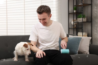 Photo of Pet shedding. Smiling man with lint roller removing dog's hair from pants at home