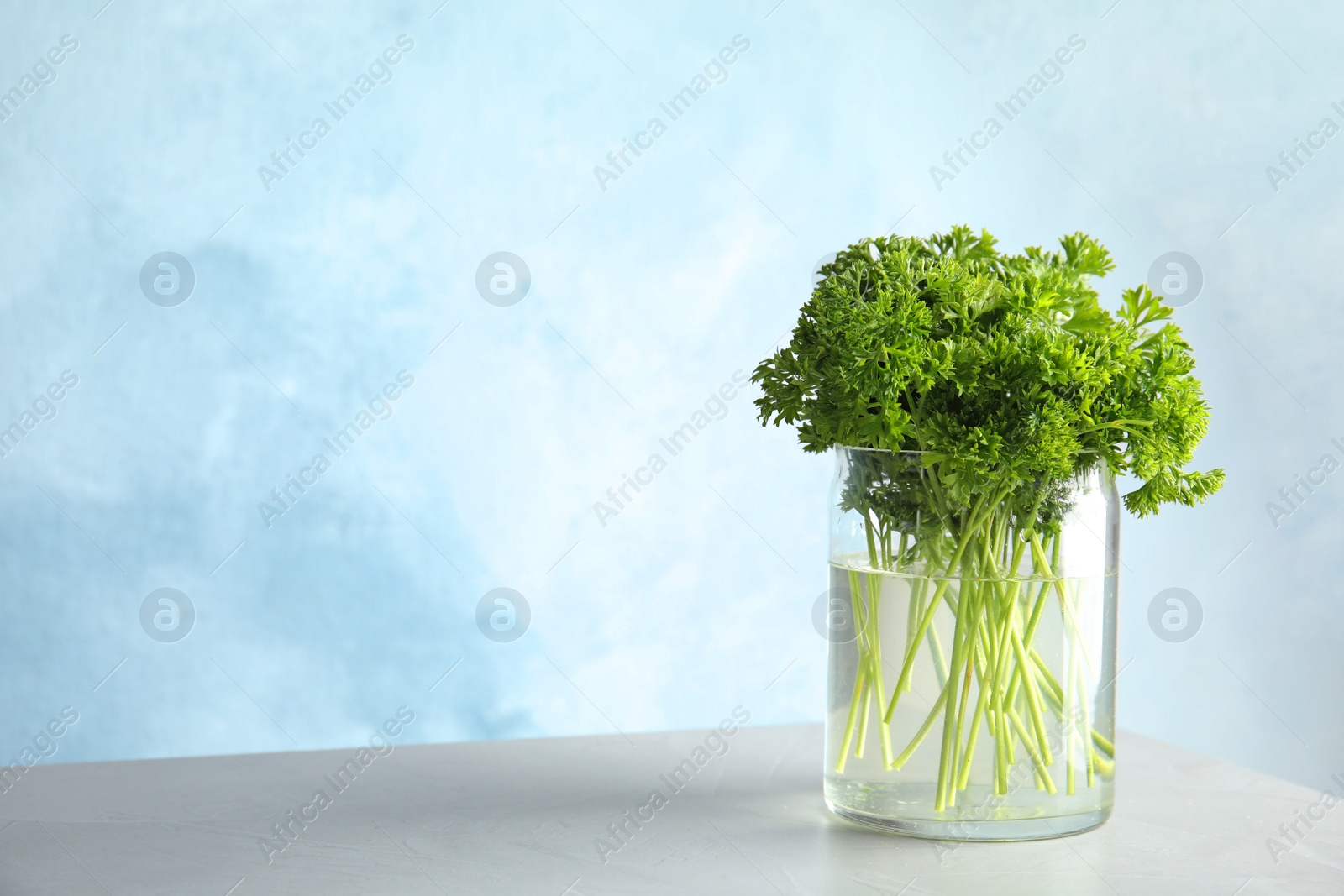 Photo of Jar with fresh green parsley on table. Space for text