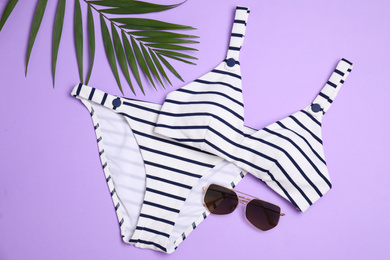 Photo of Striped bikini, sunglasses and green leaf on violet background, flat lay. Beach objects