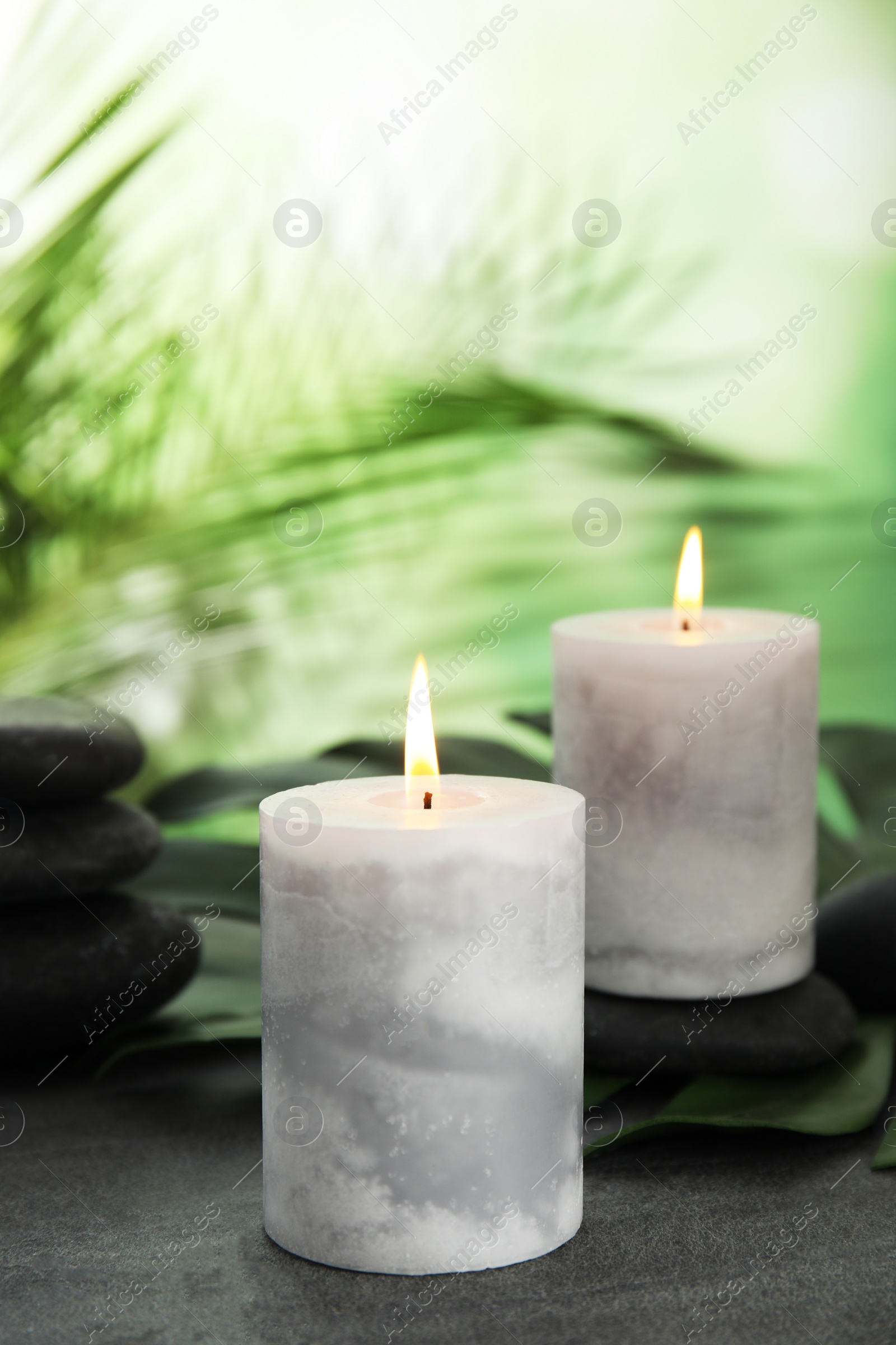 Photo of Burning candles and spa stones on grey table against blurred green background, space for text