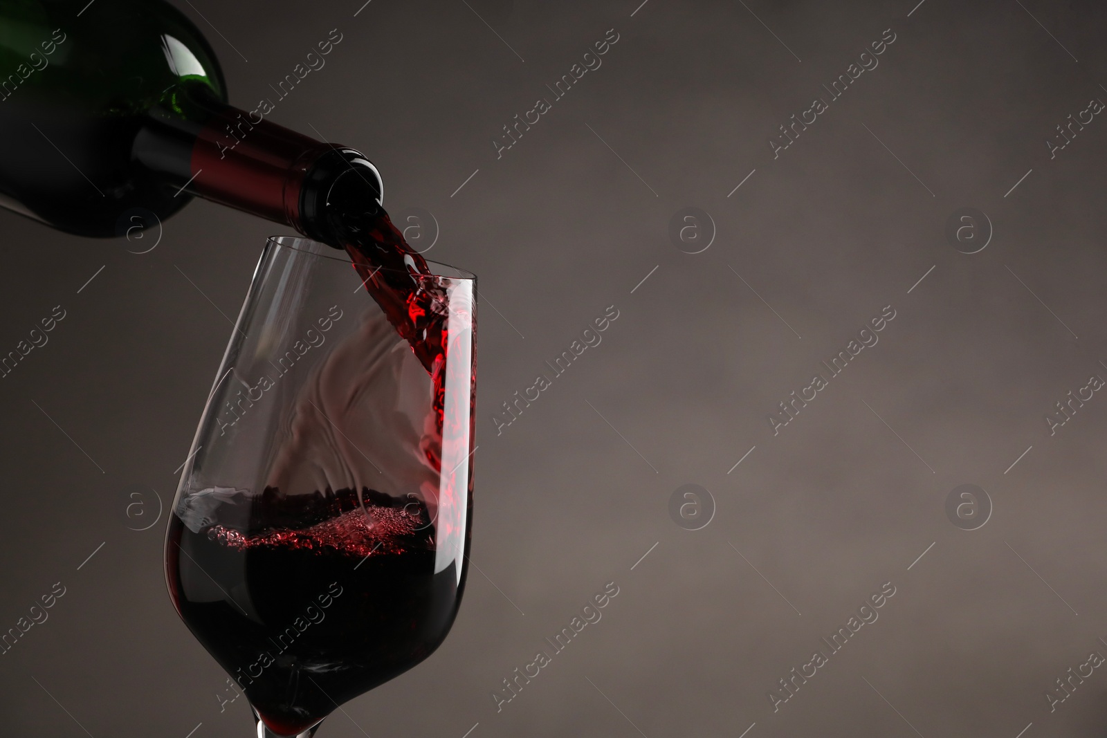 Photo of Pouring tasty red wine from bottle into glass on gray background, closeup. Space for text