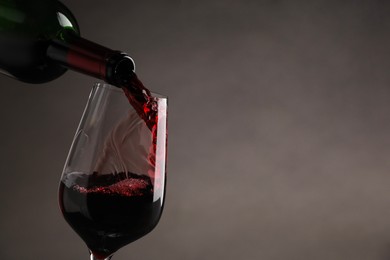 Pouring tasty red wine from bottle into glass on gray background, closeup. Space for text