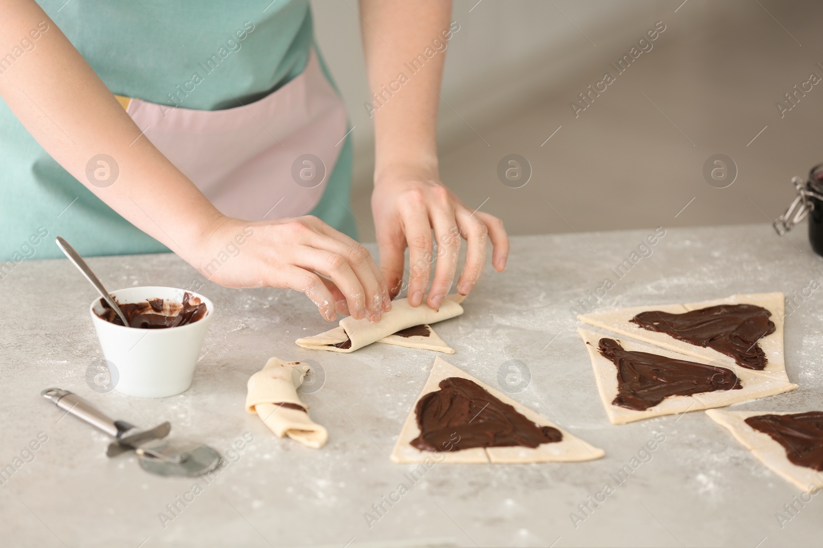 Photo of Woman preparing tasty croissants with chocolate paste on table, closeup