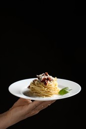 Photo of Woman holding plate of tasty spaghetti with sun-dried tomatoes and parmesan cheese on black background, closeup and space for text. Exquisite presentation of pasta dish