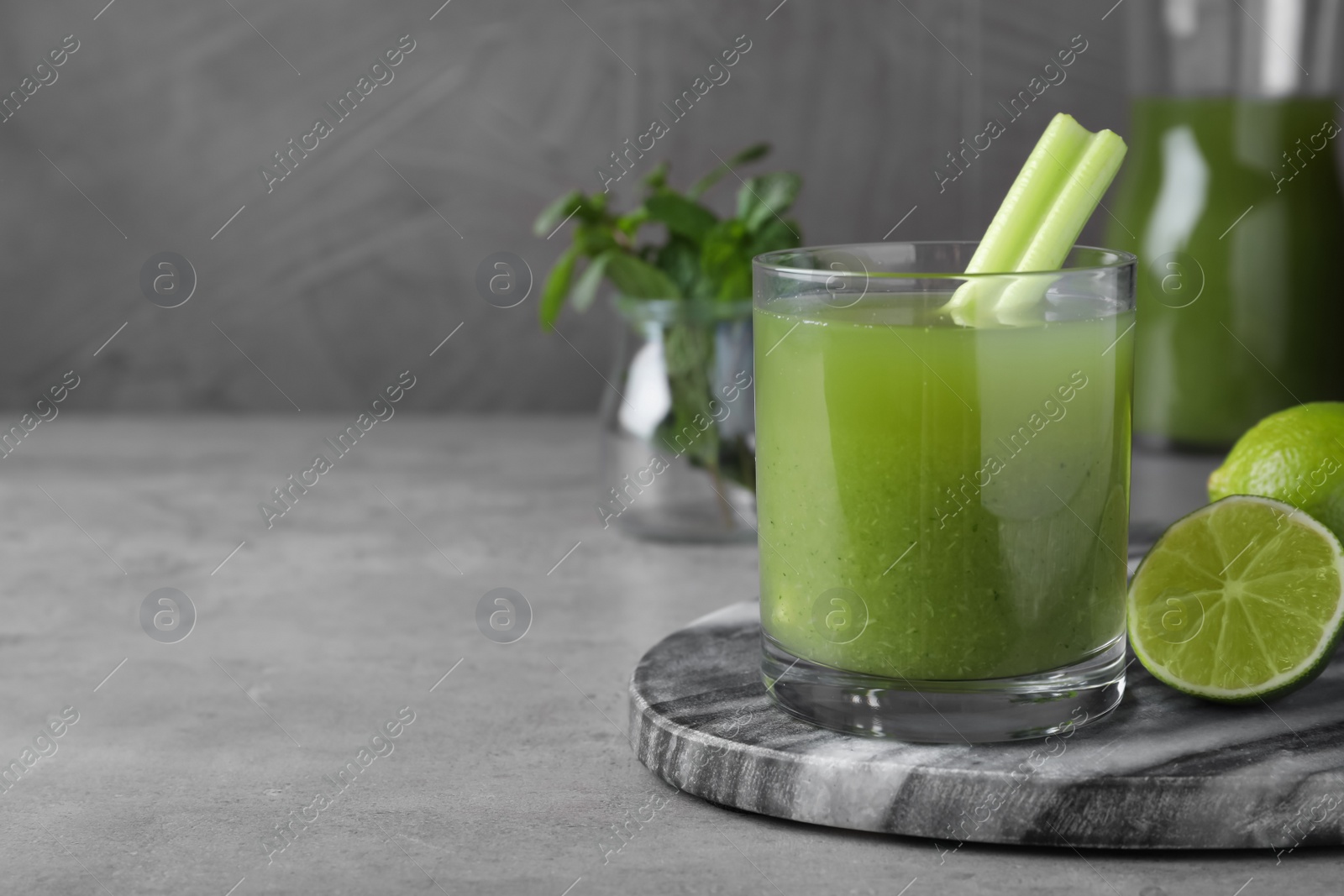 Photo of Glass of fresh celery juice and lime on grey table, closeup. Space for text