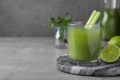 Photo of Glass of fresh celery juice and lime on grey table, closeup. Space for text