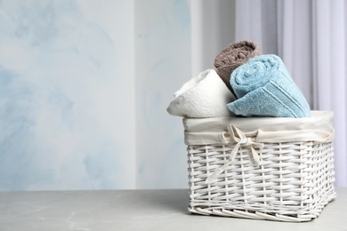 Photo of Basket with soft bath towels on table against blurred background. Space for text