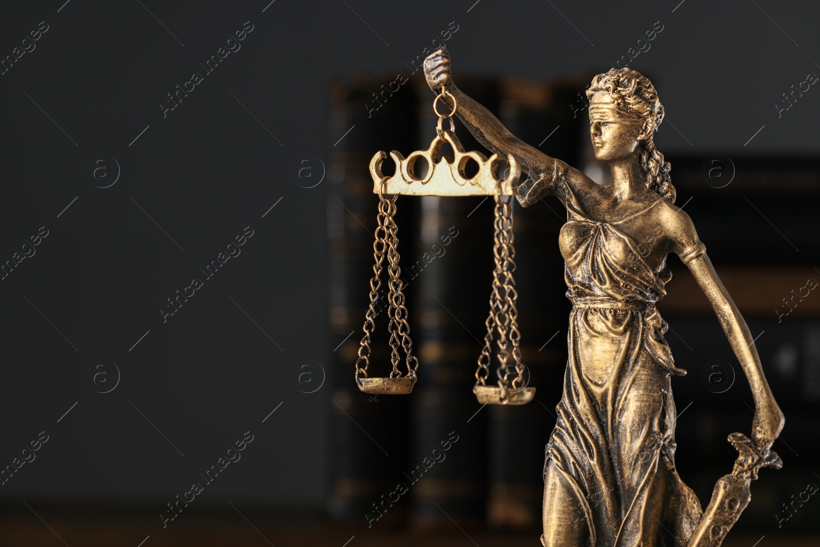 Photo of Symbol of fair treatment under law. Statue of Lady Justice and books on dark background, closeup. Space for text