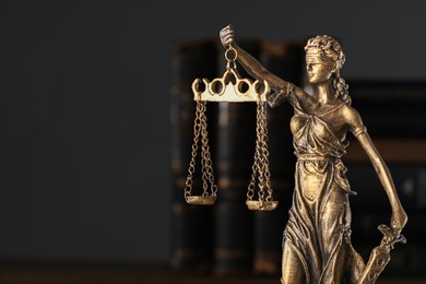 Photo of Symbol of fair treatment under law. Statue of Lady Justice and books on dark background, closeup. Space for text