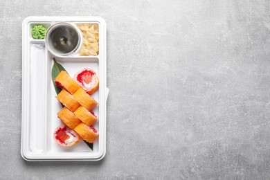 Photo of Food delivery. Delicious sushi rolls with soy sauce, ginger, wasabi, chopsticks in plastic container on light grey table, top view and space for text