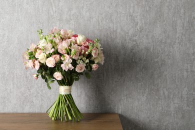 Photo of Beautiful bouquet of fresh flowers on wooden table near grey wall, space for text