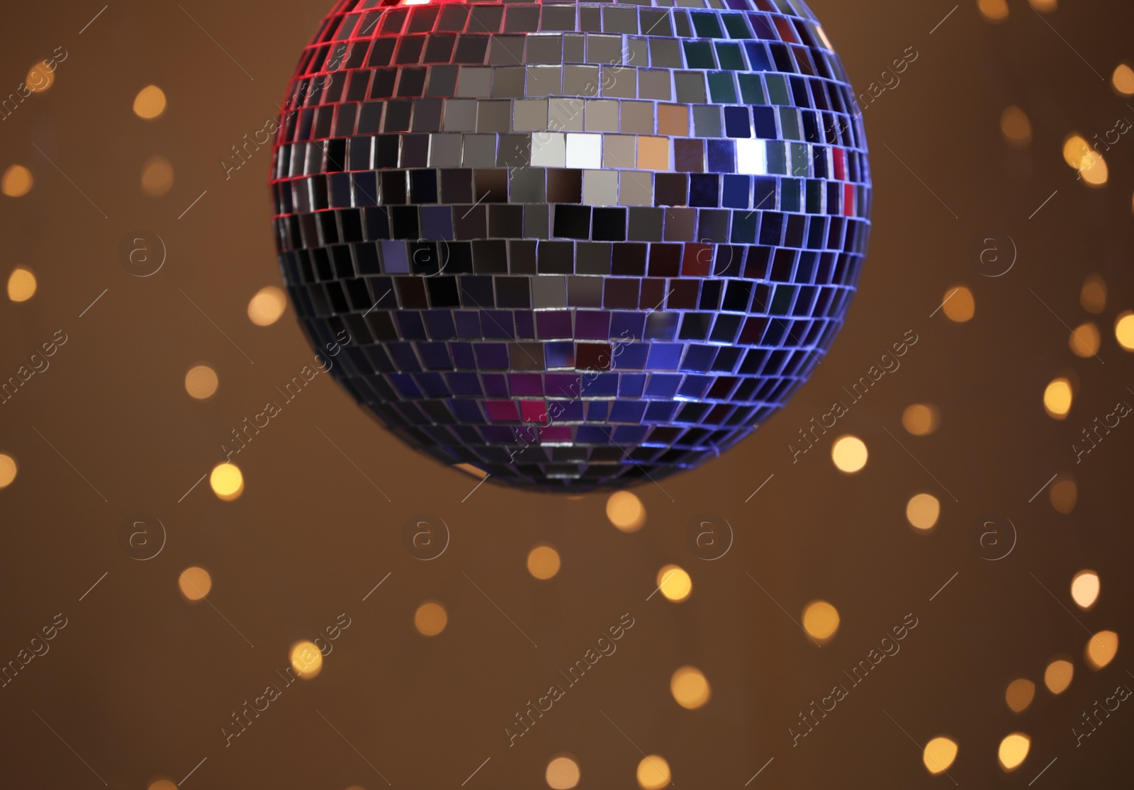 Photo of Shiny disco ball against blurred lights on brown background, closeup