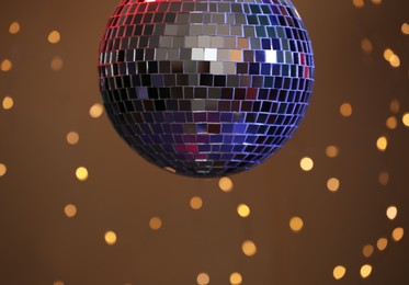 Photo of Shiny disco ball against blurred lights on brown background, closeup
