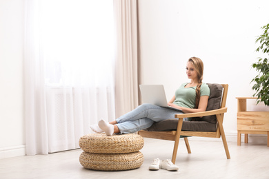 Photo of Young woman with laptop sitting in armchair at home