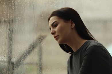 Depressed woman near window on rainy day, space for text