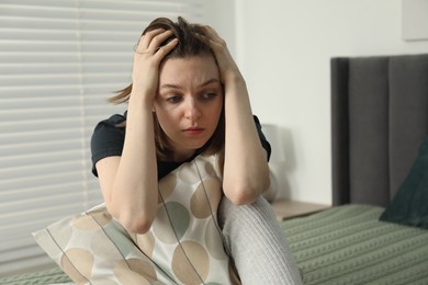 Sad young woman sitting on bed at home