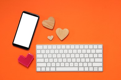 Photo of Long-distance relationship concept. Decorative hearts, smartphone and keyboard on orange background, flat lay