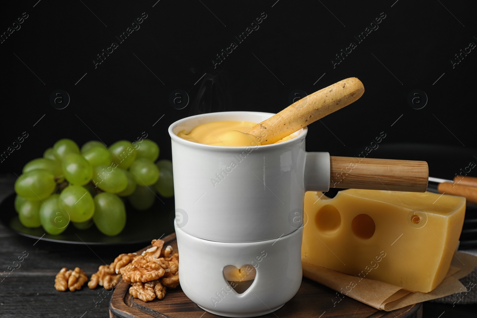 Photo of Pot of tasty cheese fondue and bread stick on black wooden table