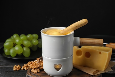 Photo of Pot of tasty cheese fondue and bread stick on black wooden table