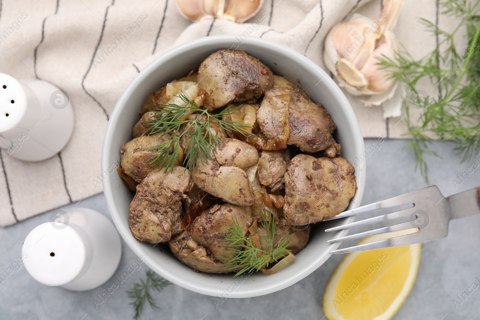 Photo of Tasty fried chicken liver with onion and dill served on grey table, flat lay