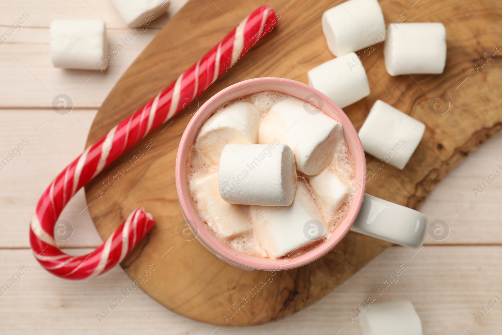 Photo of Tasty hot chocolate with marshmallows and candy cane on light wooden table, top view