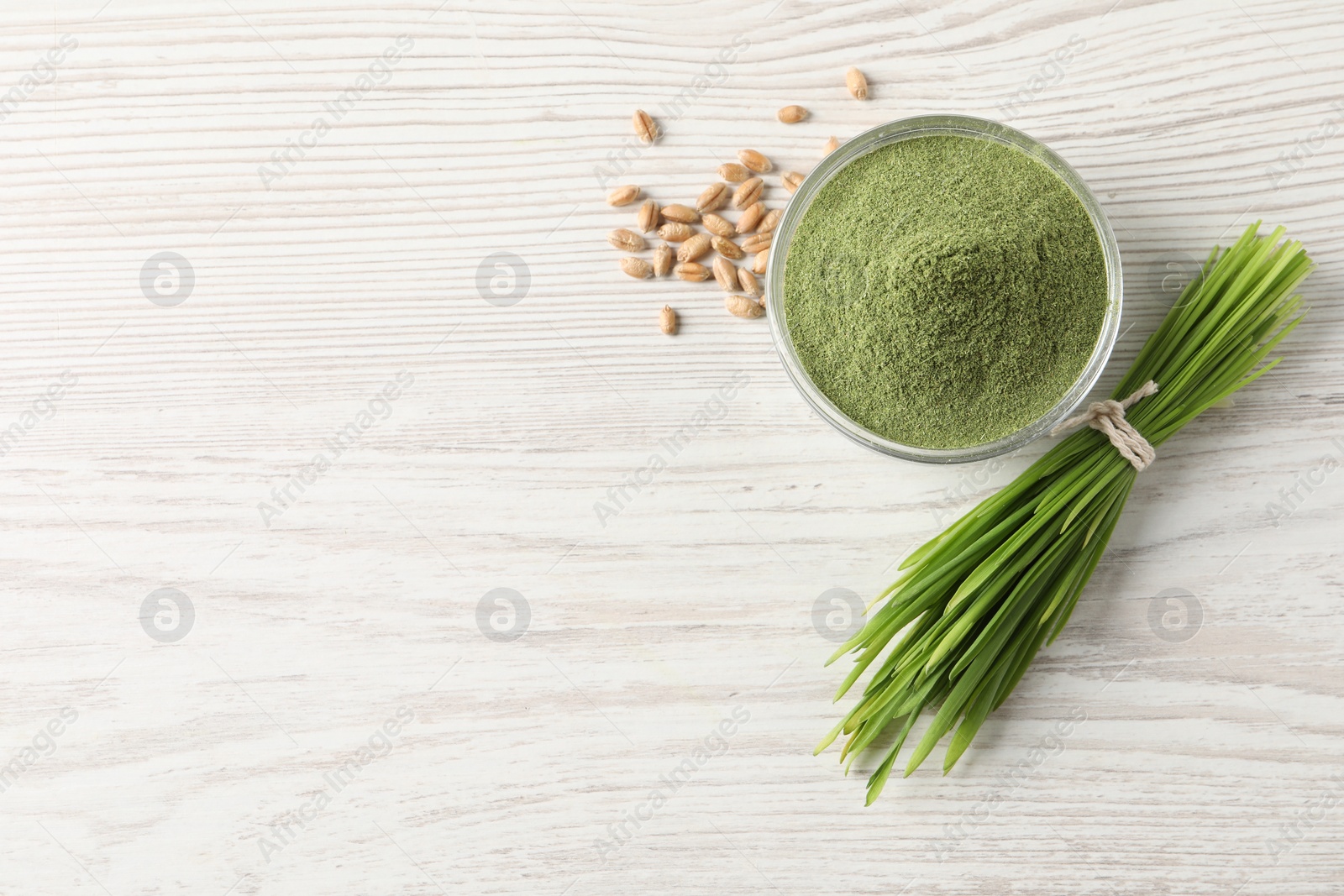 Photo of Wheat grass powder in bowl, seeds and fresh sprouts on white wooden table, flat lay. Space for text