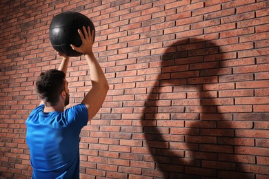 Athletic man doing exercise with medicine ball near red brick wall, space for text