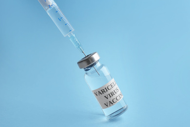 Photo of Filling syringe with chickenpox vaccine on light blue background. Varicella virus prevention