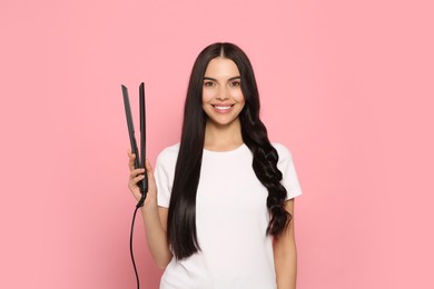 Photo of Beautiful happy woman with hair iron on pink background
