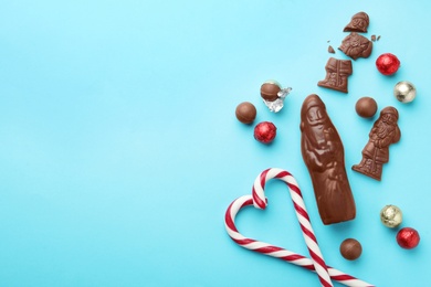 Photo of Flat lay composition with chocolate Santa Claus candies and sweets on light blue background, space for text