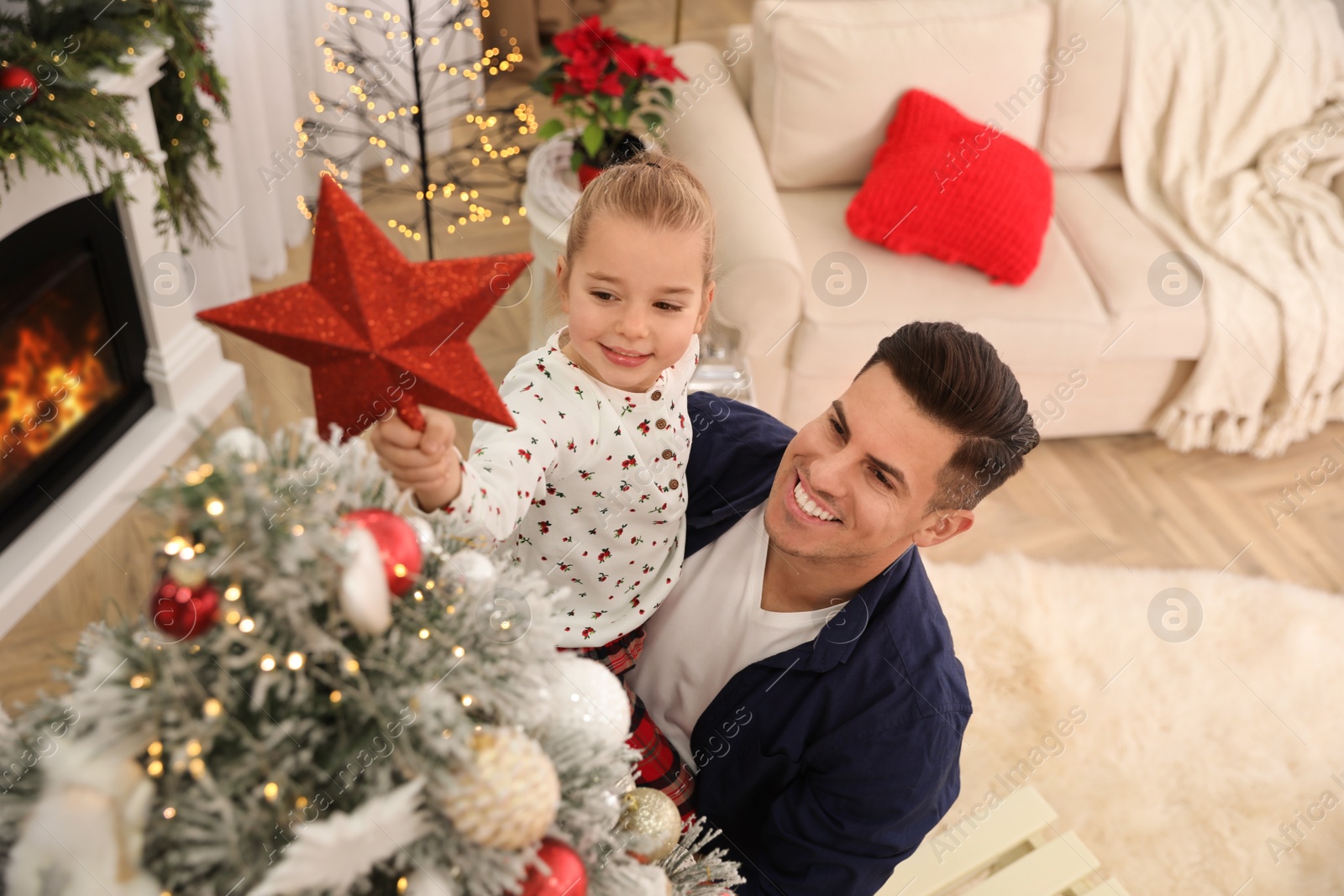 Photo of Father and little daughter decorating Christmas tree with star topper in room, above view
