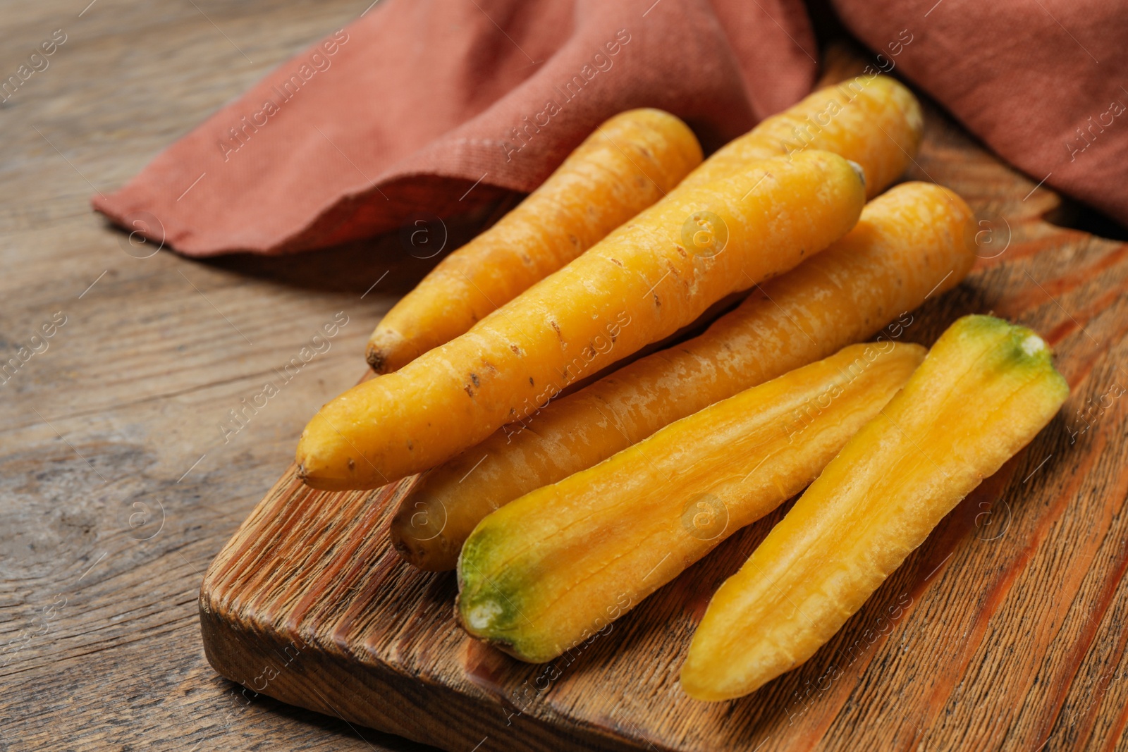 Photo of Raw yellow carrots on wooden board, closeup