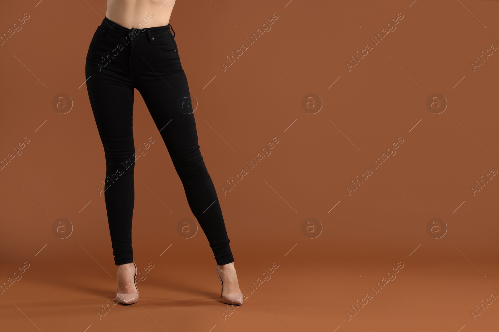 Photo of Woman wearing stylish black jeans and high heels shoes on brown background, closeup. Space for text