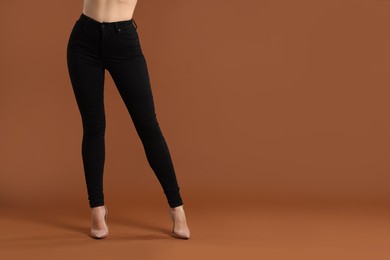 Woman wearing stylish black jeans and high heels shoes on brown background, closeup. Space for text