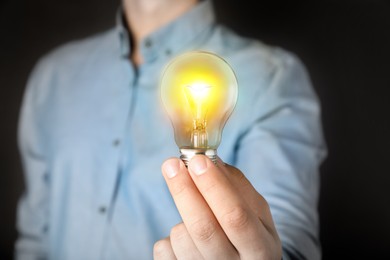 Image of Glow up your ideas. Man holding light bulb on black background, closeup