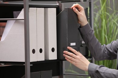 Photo of Woman taking folder with documents from shelf in office, closeup