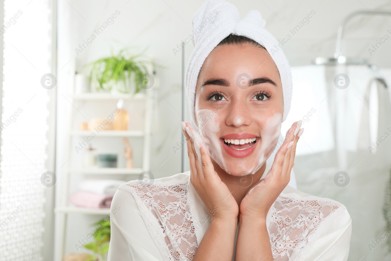 Photo of Beautiful young woman applying cleansing foam onto face in bathroom. Skin care cosmetic