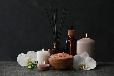 Beautiful composition with burning candles and different spa products on dark grey table