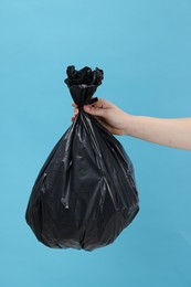 Photo of Woman holding plastic bag full of garbage on light blue background, closeup