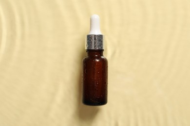 Bottle of cosmetic serum and water on beige background, top view