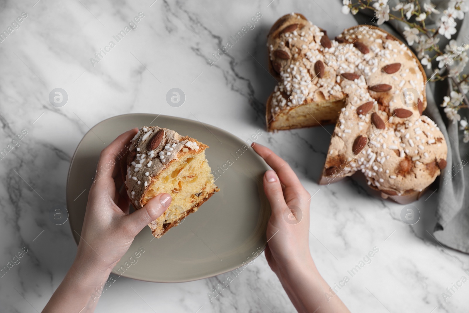 Photo of Woman with piece of delicious Italian Easter dove cake (traditional Colomba di Pasqua) at white marble table, above view