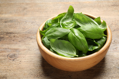 Photo of Fresh basil leaves in bowl on wooden table