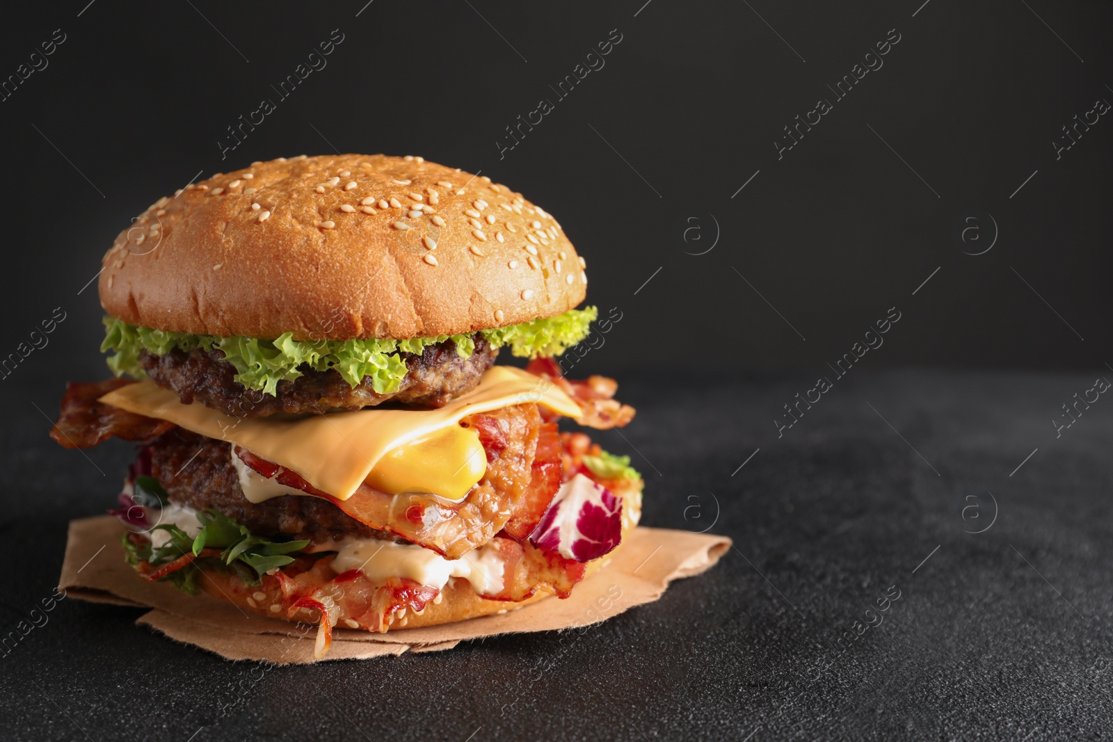 Photo of Tasty double burger with bacon on table against dark background