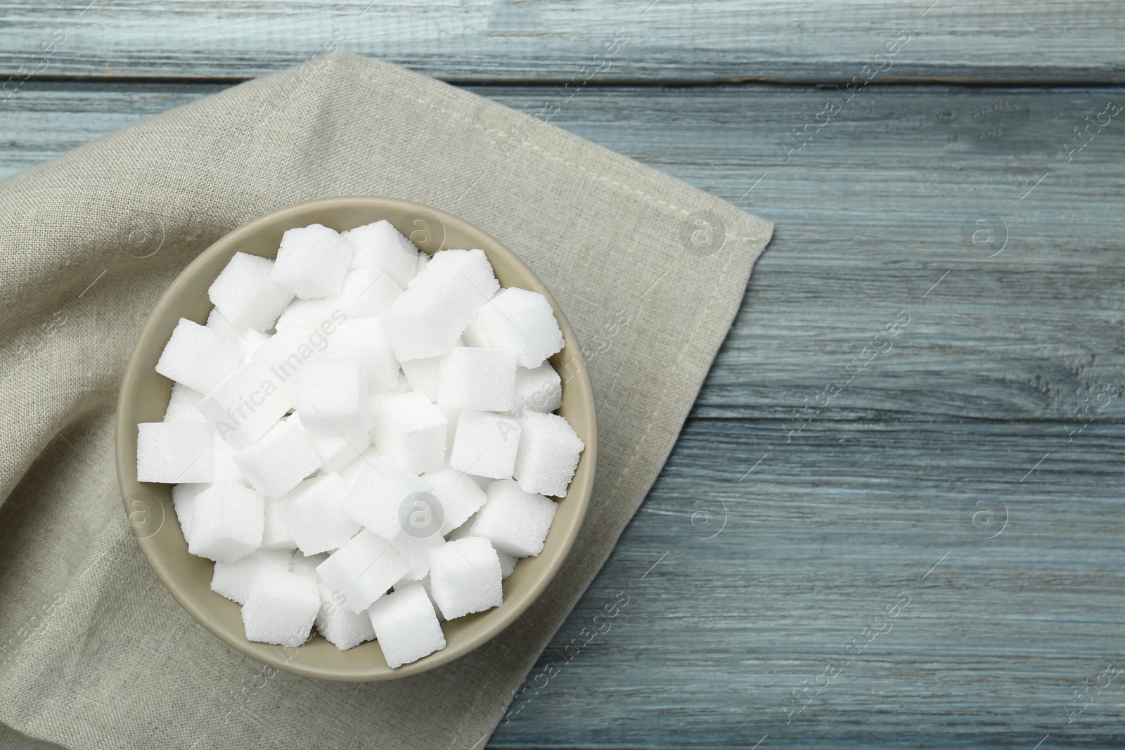 Photo of White sugar cubes in bowl on wooden table, top view. Space for text