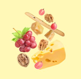 Cheese, breadstick, grapes and walnuts falling against pale light yellow background