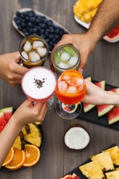 Photo of Friends clinking glasses with cocktails at wooden table, top view