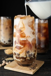 Pouring milk into glass with bubble tea on black wooden table, closeup
