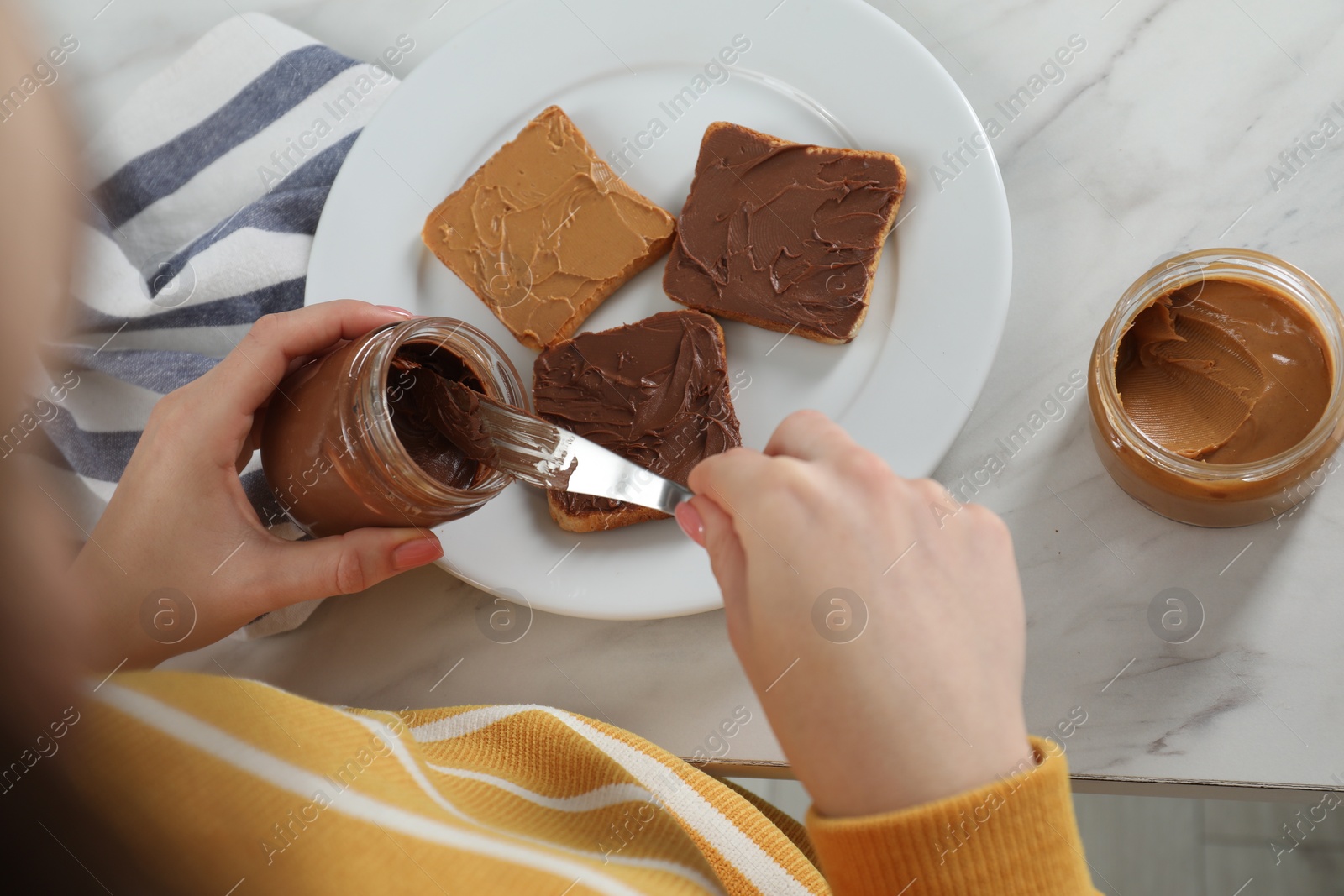 Photo of Woman taking tasty nut butter onto knife at marble table, above view